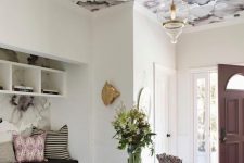 a chic entryway with a ceiling done with mauve floral wallpaper that echoes with the door and pillows