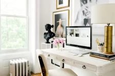 a chic glam home office in creamy shades, with a vintage desk, a creamy and gold chairs, a statement gallery wall and a table lamp