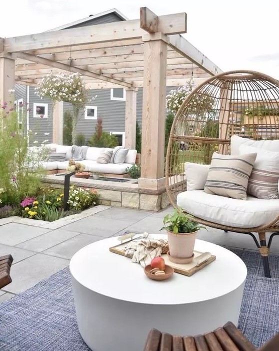 a chic neutral modern outdoor space with a corner sofa, a rattan chair, wooden chairs, a round concrete table