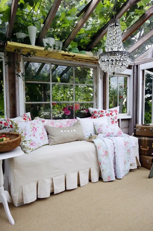 a chic vintage sunroom with greenery all around, a crystal chandelier, neutral furniture and floral textiles