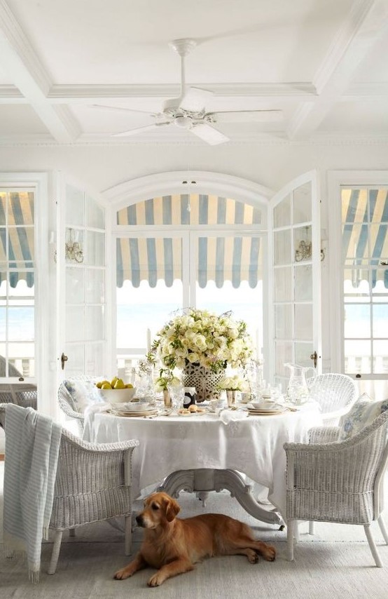 a classic vintage sunroom done in all neutrals, with a white wicker furniture set, potted blooms and neutral textiles