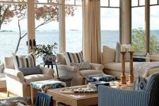 a coastal sunroom in rustic style with neutral and blue furniture, a wooden table with baskets and a vintage chandelier