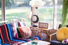a colorful boho and mid-century sunroom with a cool view, with furniture with bright textiles, pillows, rugs and some pretty potted plants is a cozy and cool space
