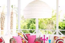 a colorful boho sunroom with a sectional and lots of colorful pillows, a low coffee table and a pendant lamp