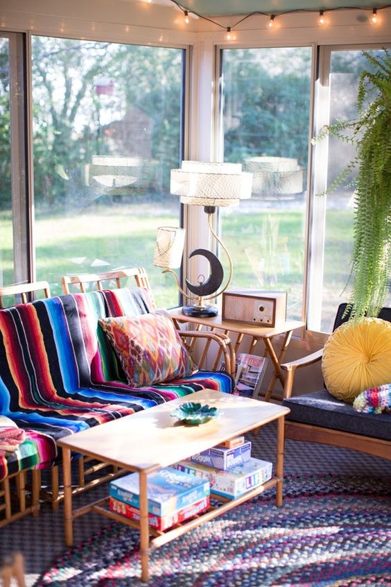 a colorful boho sunroom with rattan furniture, colorful upholstery and pillows, a coffee table and some string lights