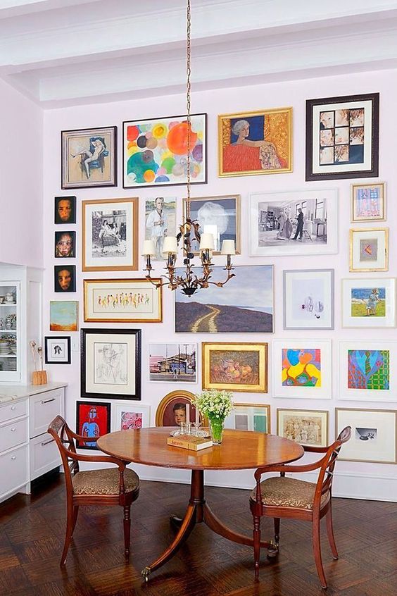 a colorful floor to ceiling gallery wall, a vintage rich-stained table and matching vintage chairs, a chic chandelier over the space