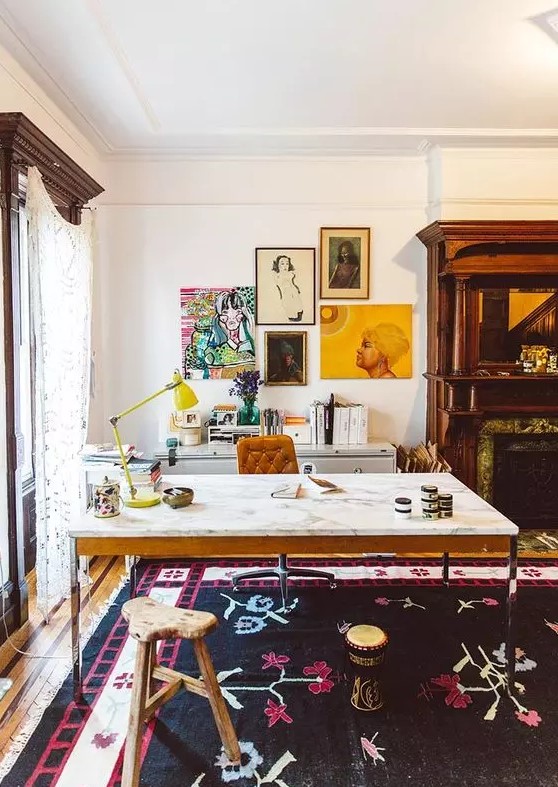 a colorful home office with a marble desk, a leather chair and a wooden stool, a built in fireplace, a credenza, a colorful gallery wall