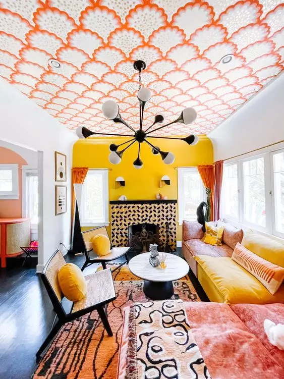 a colorful living room with a yellow accent wlal, a bold wallpaper ceiling, a pink and yellow sofa, rattan chairs and yellow pillows