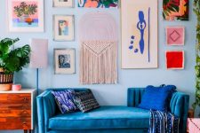 a colorful living room with lots of blue, with a bright and catchy gallery wall that includes macrame is wow