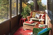 a colorful sunroom with extensive glazing, bright wicker furniture, bright pillows and a rug and some plants plus cool views of the forest