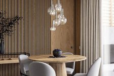 a contemporary dining space with a wood slat accent wall, a round wooden table, grey chairs, a cluster of pendant lamps