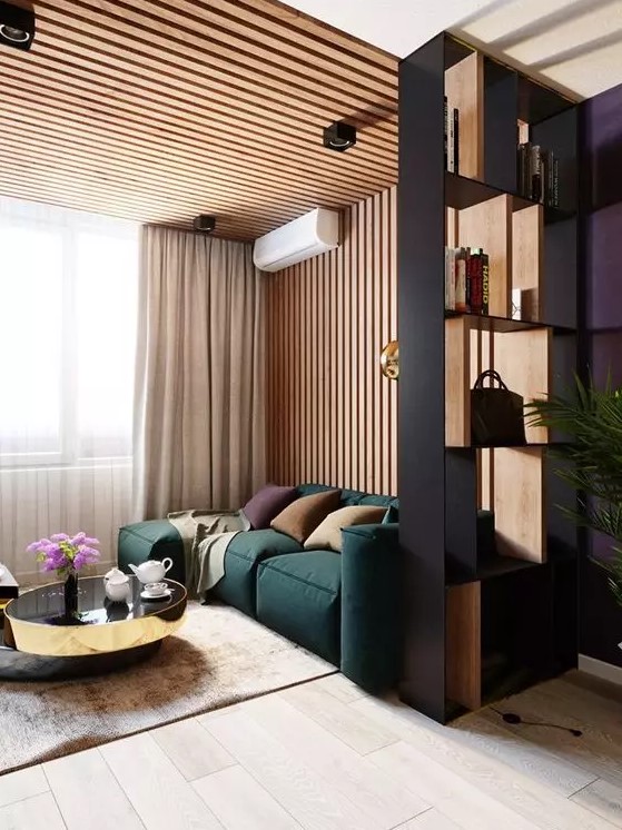 a contemporary living room with a wood slat accent wall, a green low sofa, elegant and shiny coffee tables and a shelving unit space divider