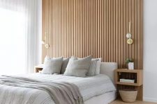 a contemporary neutral bedroom with a wood slat accent wall, a neutral upholstered bed with neutral bedding, floating nightstands