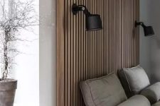 a contemporary neutral bedroom with a wood slat accent wall that features a couple of sconces, a grey upholstered bed and grey bedding, a potted plant