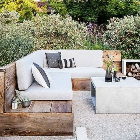a contemporary terrace with a built-in bench with neutral upholstery and printed pillows, a concrete coffee table and firewood storage