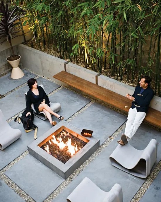 a contemporary terrace with a concrete fire pit, concrete loungers, a floating wooden bench and tall bamboo feels very edgy and cool
