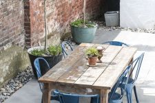a cool and simple outdoor rustic dining space with a shabby chic table, blue metal chairs, potted plants and pebbles