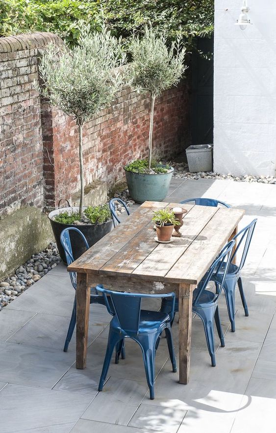 a cool and simple outdoor rustic dining space with a shabby chic table, blue metal chairs, potted plants and pebbles