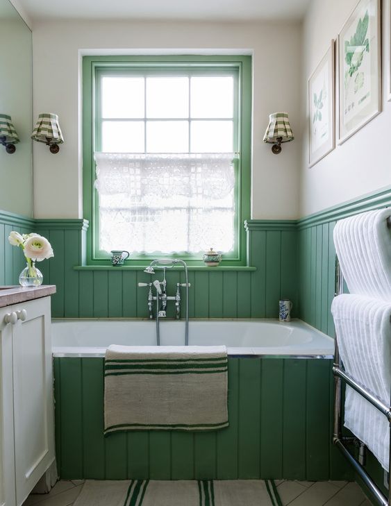 a cool green bathroom with planked walls and a bathtub, a neutral vanity, a couple of botanical artworks on the wall