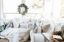 a cozy neutral farmhouse sunroom with white furniture, baskets, a shabby chic table, a leaf wreath and white pumpkins