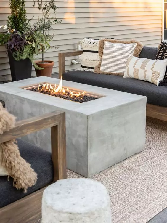 a cozy outdoor zone with black sofas and pritned pillows, a concrete fire table and side tables plus potted plants