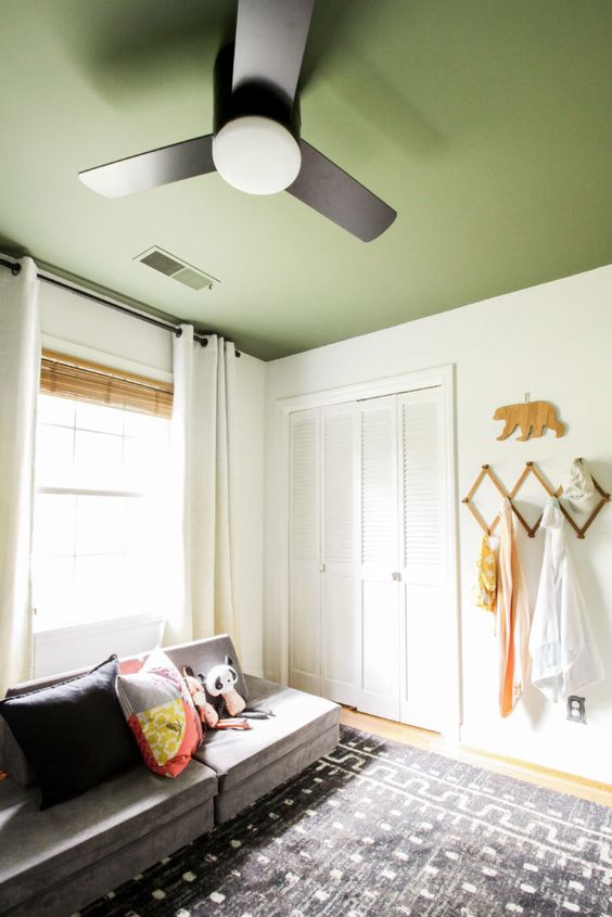 a cozy room with creamy walls and a grass green ceiling, a low grey sofa and a printed rug and a fan on the ceiling