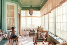 a cozy vintage sunroom in green and neutrals, wicker and wooden furniture, floral textiles, a pendant lamp and lots of sunlight