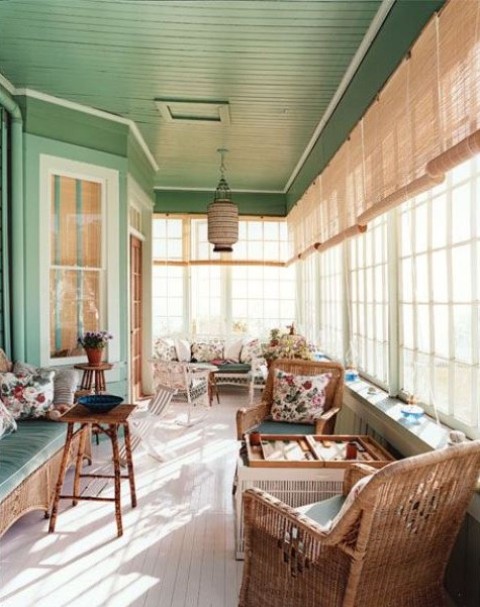 a cozy vintage sunroom in green and neutrals, wicker and wooden furniture, floral textiles, a pendant lamp and lots of sunlight