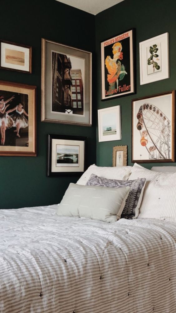 a dark green bedroom with a bed and printed bedding plus a catchy two wall gallery wall with vintage artwork and posters