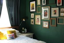 a dark green bedroom with a white bed with neutral bedding and neutral nightstands, a gallery wall of vintage artwork and empty frames