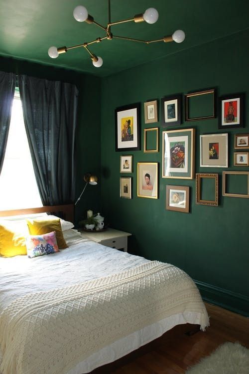 a dark green bedroom with a white bed with neutral bedding and neutral nightstands, a gallery wall of vintage artwork and empty frames