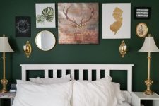 a dark green bedroom with white furniture, white bedding, elegant and chic table lamps and a catchy gallery wall with a mirror and some artwork