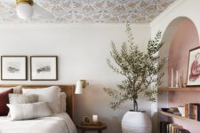 a delicate bedroom with a wallpaper ceiling, an arched niche with shelves, a rattan bed with neutral bedding