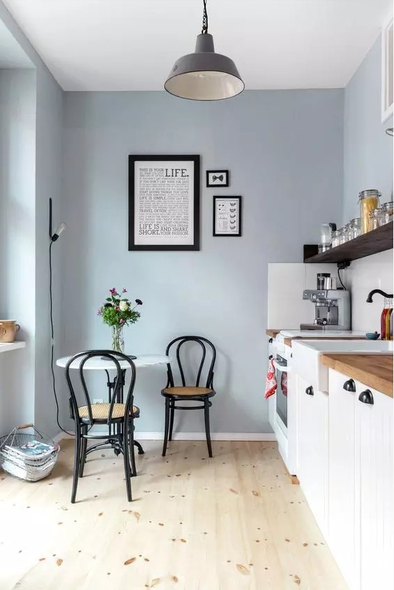a dusty blue kitchen with white cabinets, an open shelf, a round table, black chairs and a pendant lamp, a mini gallery wall