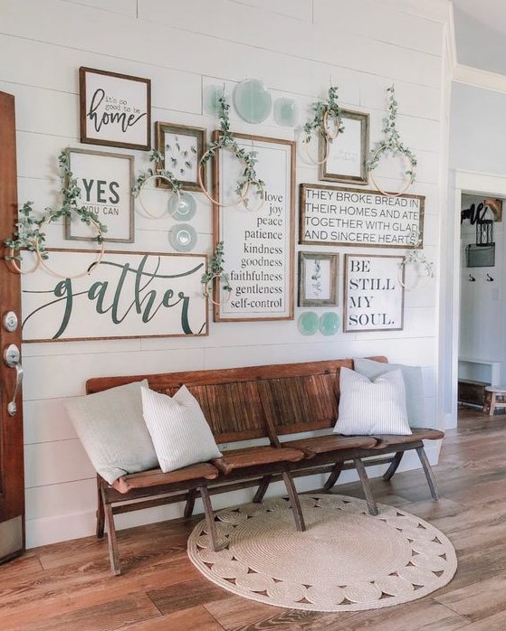 a farmhouse gallery wall with framed signs and artworks, greenery wreaths and blue porcelain plates is cool
