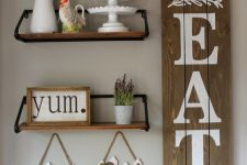 a farmhouse kitchen gallery wall with a wooden sign, some animal silhouettes, shelves with potted plants and framed signs