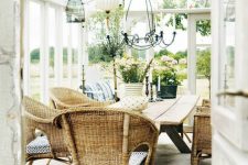 a farmhouse sunroom dining room with a table, wicker chairs, a vintage chandelier and some blooms and greenery
