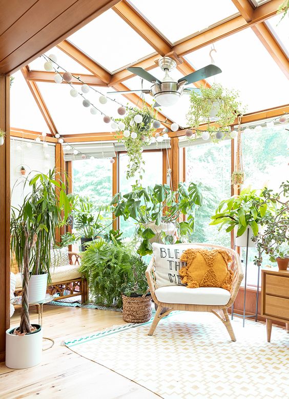 a glazed boho sunroom with rattan furniture, potted plants, string lights and a printed rug feels ethereal and light filled