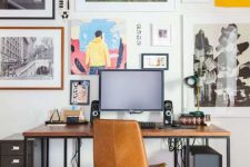 a home office with a sleek desk with black metal framing, a black file cabinet, a colorful gallery wall and an amber leather chair