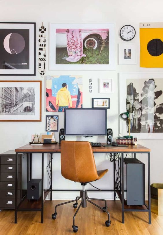 a home office with a sleek desk with black metal framing, a black file cabinet, a colorful gallery wall and an amber leather chair