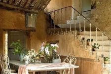 a large farmhouse table and white forged chairs, a large lantern over them, a watering can and some greenery and blooms to highlight that refined French feel