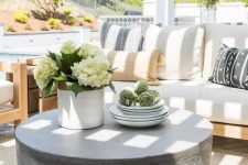 a light-filled terrace with a neutral sofa with printed pillows, a chair, a round concrete coffee table and some blooms