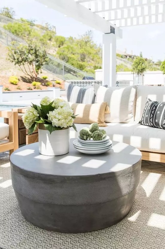 a light-filled terrace with a neutral sofa with printed pillows, a chair, a round concrete coffee table and some blooms