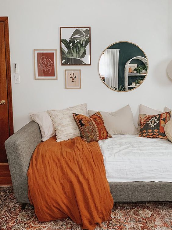 a lovely boho guest bedroom with a mini gallery wall, a round mirror, a daybed with lots of pillows is welcoming