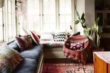 a lovely boho sunroom space with a large built-in sofa and colorful upholstery and pillows, a bold printed rug and a chair