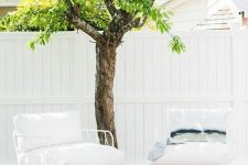 a lovely deck with white metal chairs finished with white cushions, a white coffee table, a living tree right in the deck
