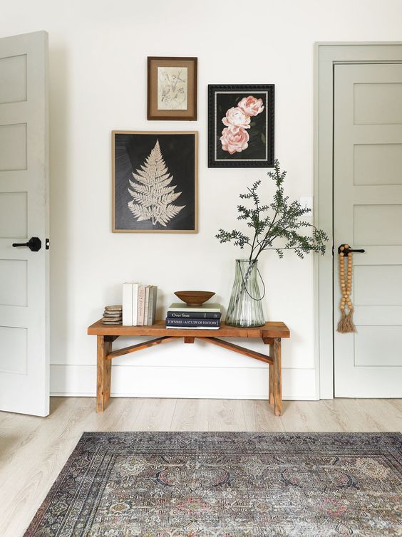 a lovely farmhouse entryway with a stained bench, a mini gallery wlal, some books and a plant in a vase is all cool