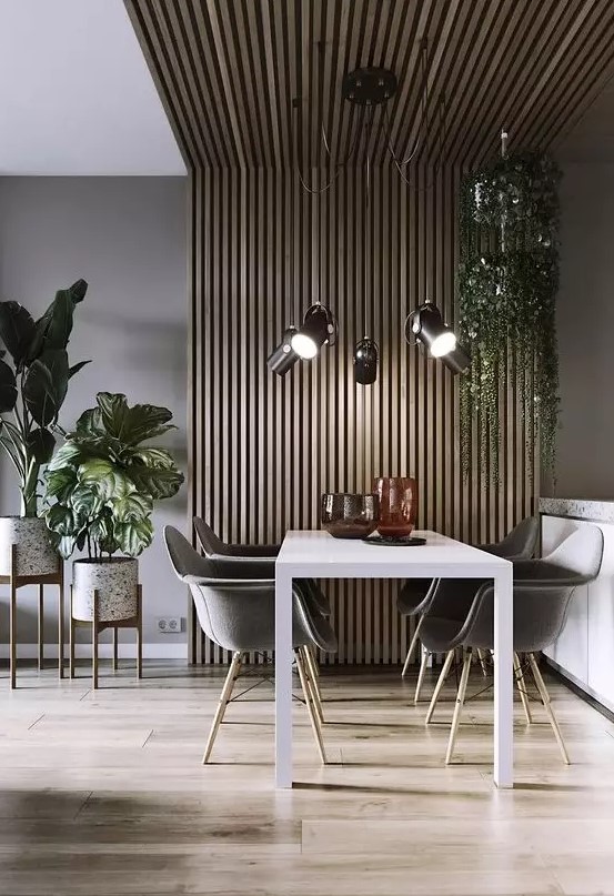 a lovely mid century modern dining space with a wood slat accent wall and ceiling, a white table, grey chairs and lots of plants