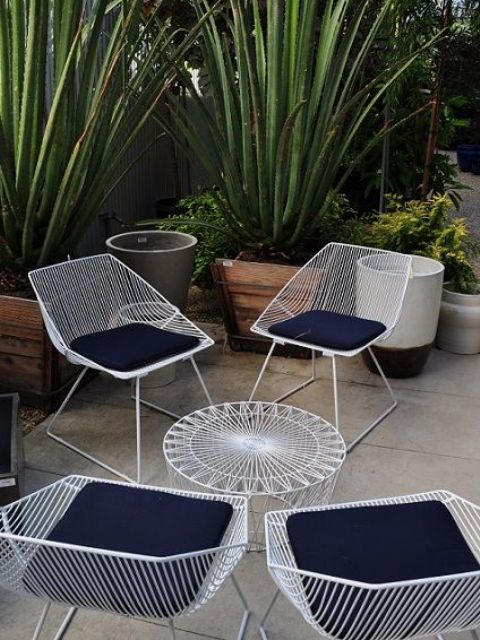 a lovely outdoor lounge zone with a white metal table and chairs, navy cushions and potted plants around is cool