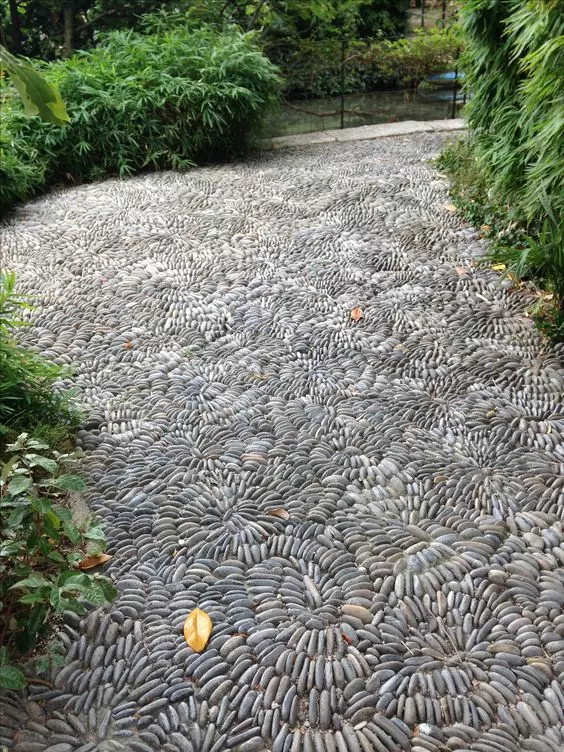 a lovely pebble garden path with swirl and flower patterns and greenery around it is a col idea for a natural space